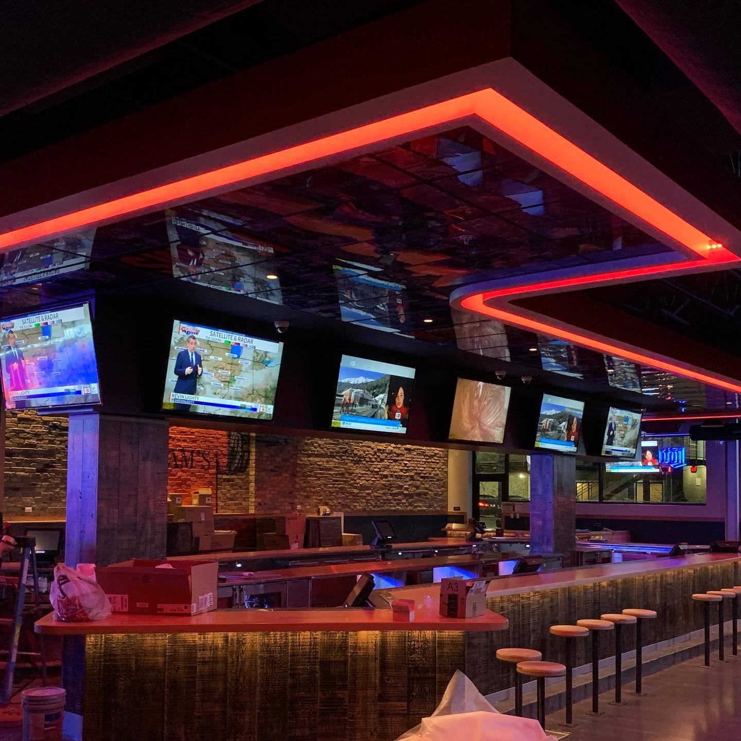 Image: View of a bar with stool seating on the right. There are six televisions above the bar. Photo from KAM's Facebook page.