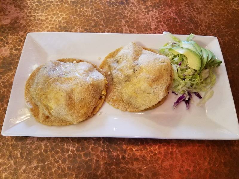 Image: Two gorditas and a small avocado salad sit on a rectangular white plate. The gorditas are round and a light golden color. The plate sits on a hammered copper table. Photo by Matthew Macomber. 