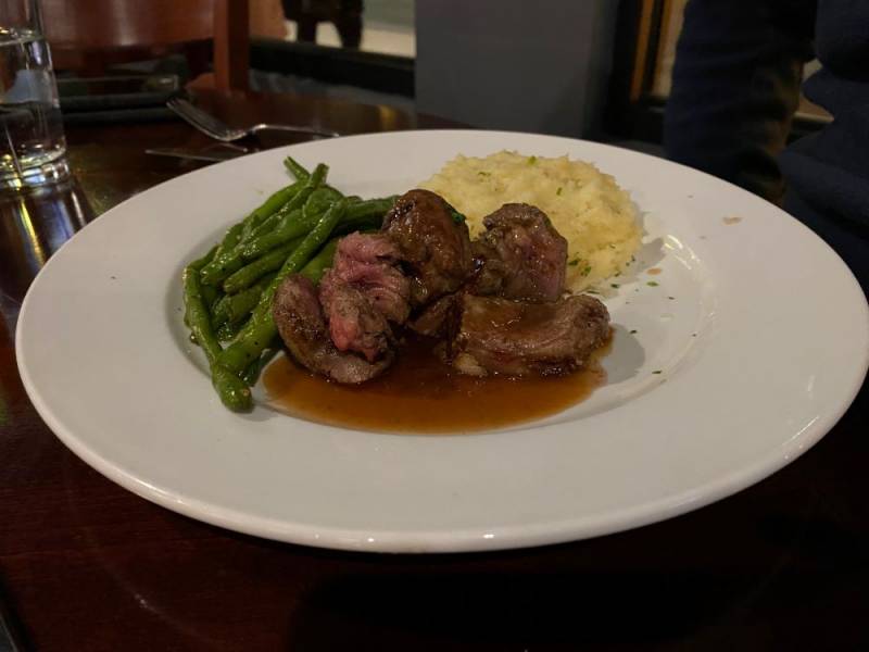 Image: A round white plate sits on a dark wood table. There are five pieces of steak in a dark brown sauce. The steak is surrounded by mashed potatoes and green beans. Photo by Julie McClure.