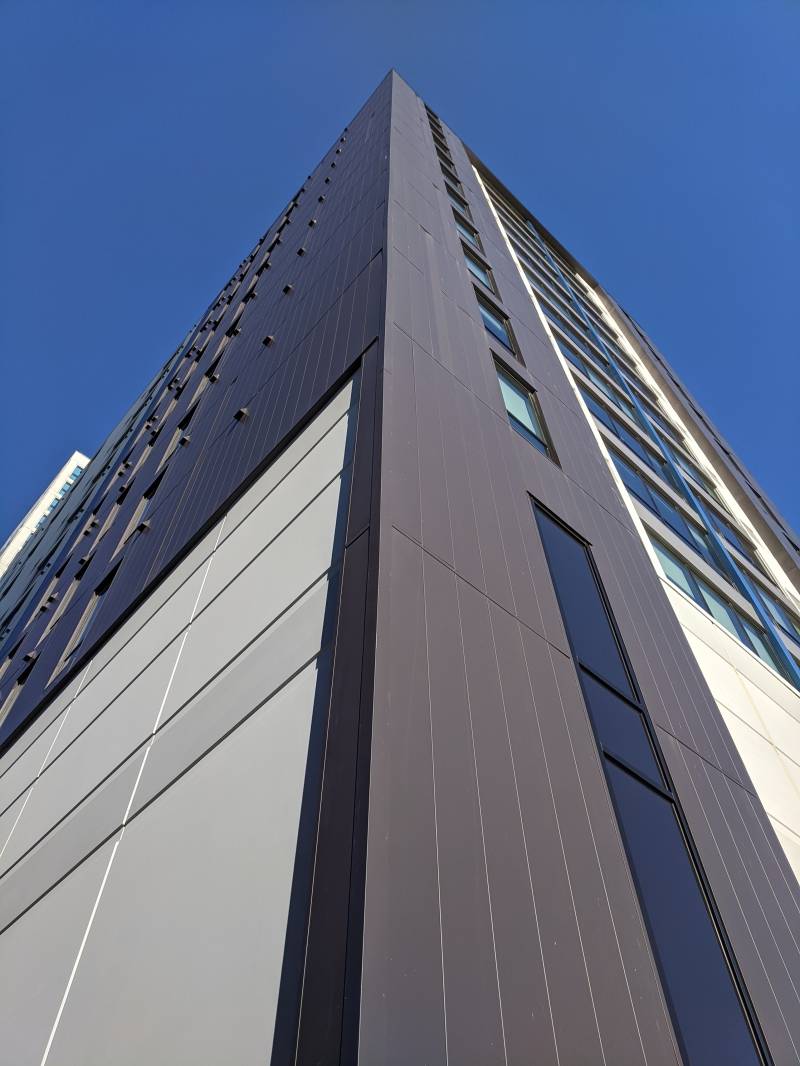 Image: A view of the corner of the building looking up from the ground. The background is blue sky.