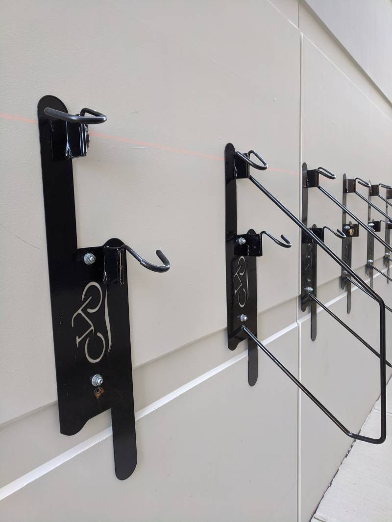 Image: A close up few of the black bike hooks attached to a white wall. They each have a hook and a metal loop, the first one is missing the loop.