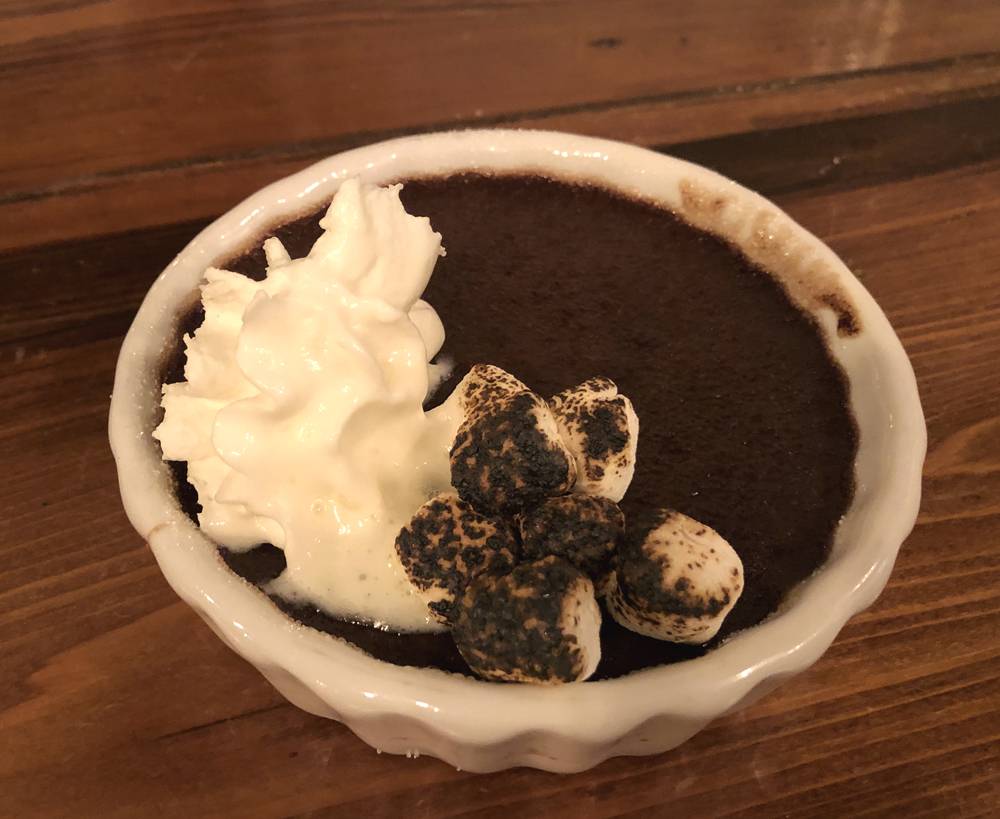 Image: Spiced hot chocolate crÃ¨me brulee dessert at the WheelHouse is garnished with whipped cream and several small, charred marshmallows. The crÃ¨me brulee is a rich, dark brown, and served in a small round bowl. The bowl sits on a wood table. Photo by Jessica Hammie.
