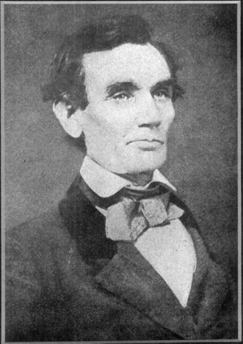 Image: A black and white photo of Abraham Lincoln. He has dark hair and no beard. He is wearing a dark suit jacket with a white shirt and light colored bow tie. 