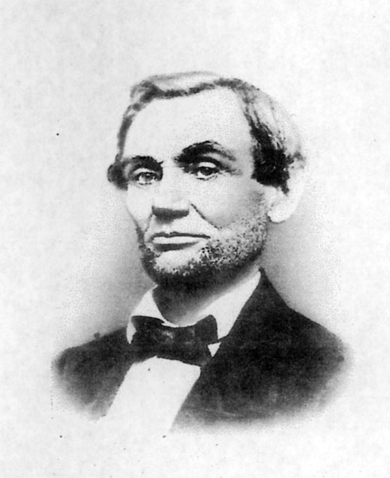 Image: A black and white photo of Abraham Lincoln. It has a white background and Lincoln is framed in a vignette. He has a beard and is wearing a dark jacket, white shirt, and dark bowtie. Photo by Samuel Alschuler.