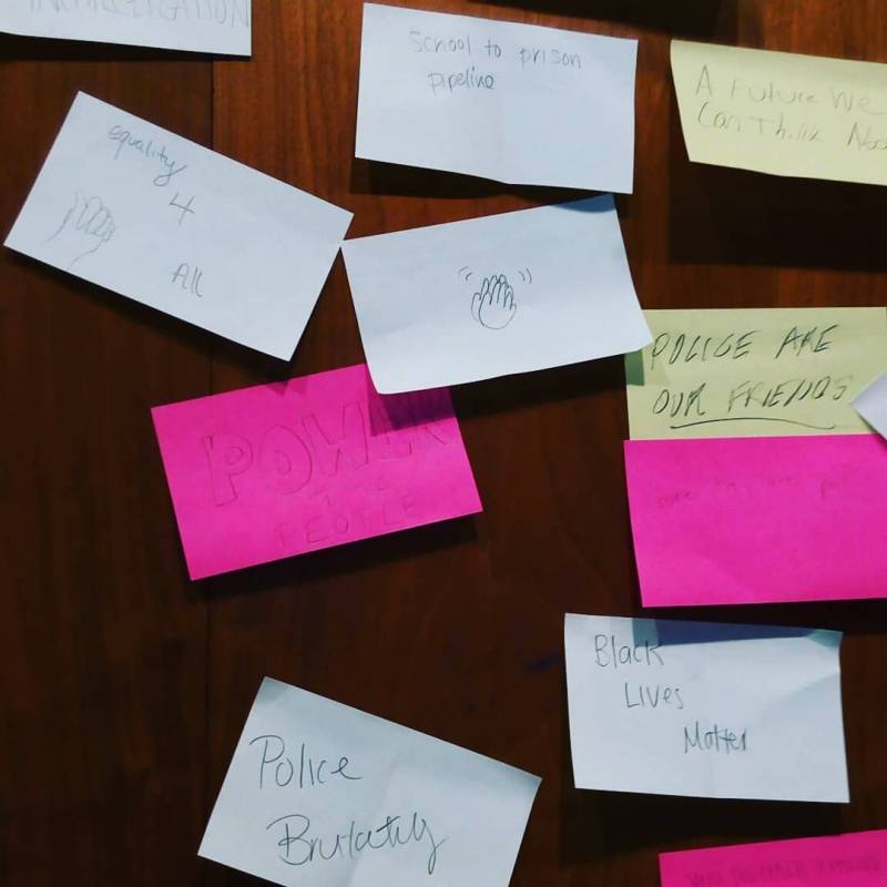 There are several white, yellow, and pink sticky notes with thoughts written on them: power to the people, police brutality, black lives matter, liberty 4 all, school to prison pipeline, police are our friends. Photo from Krannert Art Museum Facebook page. 
