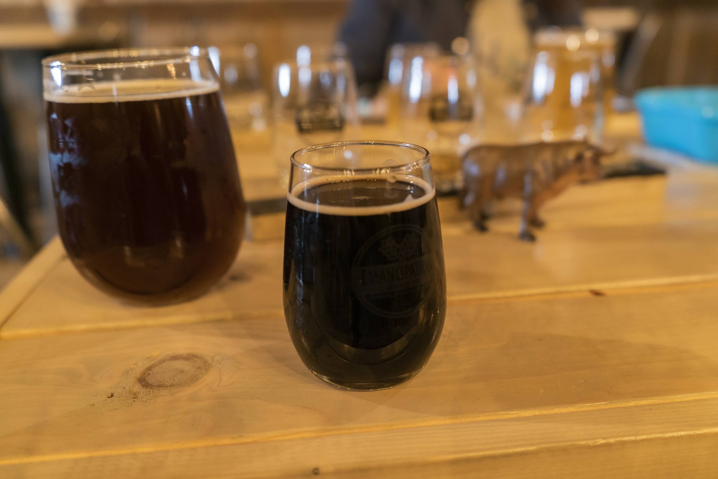 A small tumbler glass filled with a dark liquid sits on a light wood table. Behind it is a larger tumbler glass filled with a reddish brown liquid. Beer from Emancipation Brewing. Photo by Jordan Goebig. 