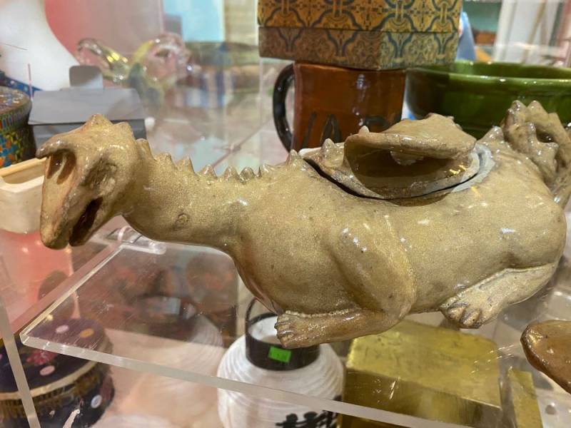 Image: A ceramic brownish-gray dragon. It appears to be hollow, and has a lid that can be lifted off by grabbing the dragon's wing. Photo by Julie McClure.