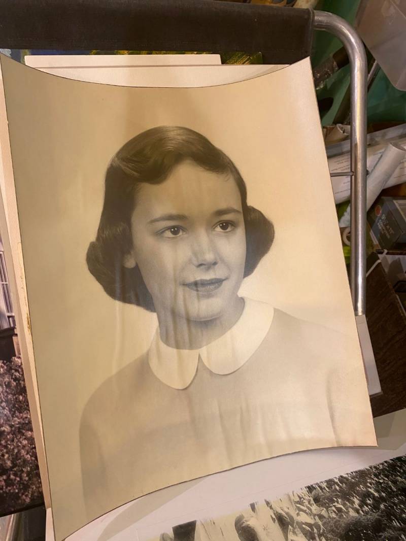 Image: A large black and white portrait of a young girl with dark hair. She is wearing a light colored shirt with a white peter pan collar. Photo by Julie McClure.