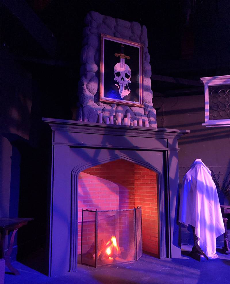 Image: Photo of dark room with lit fireplace a ghost figure to the left. Photo by Linda Evans.