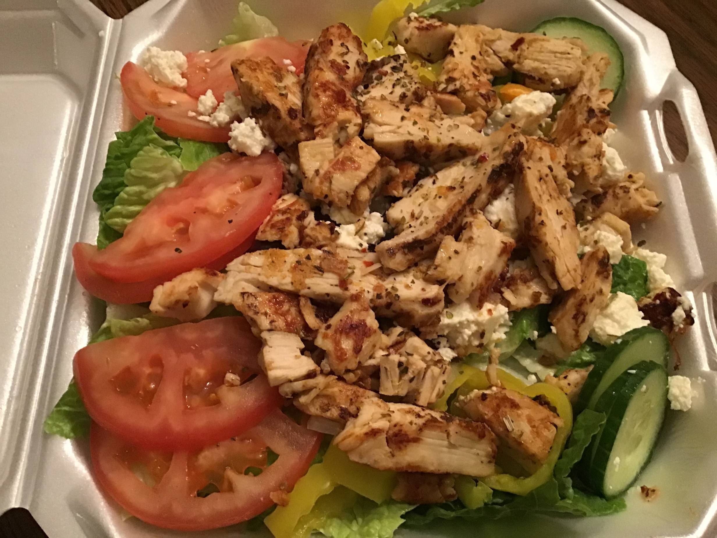Greek Salad with chicken at Niro's Gyros. A large salad is served in a white styrofoam containter. Romaine lettuce, sliced tomato, sliced cucumber, banana peppers, feta cheese, and grilled chicken are visible. Photo by Rachael McMillan. 