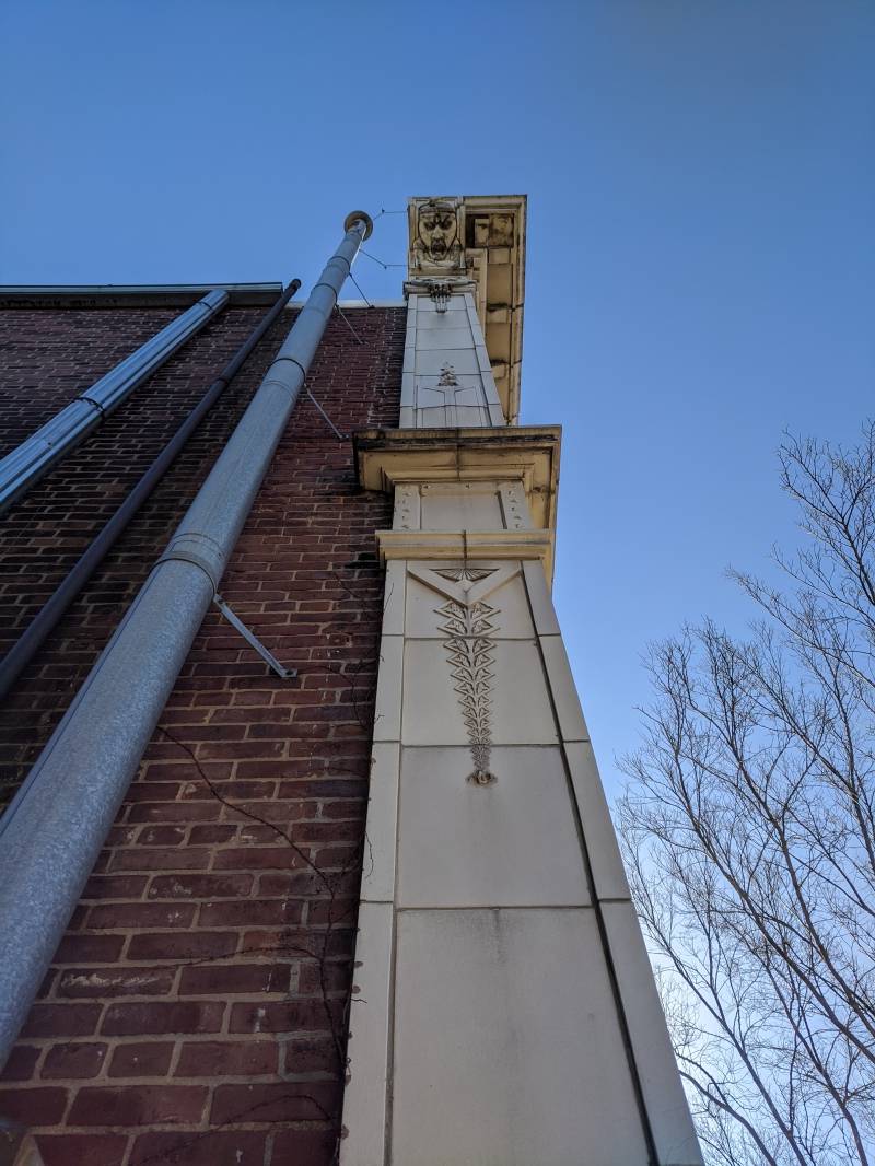 Image: The corner of a brick building. A decorative column runs up the corner, with a face carved into the underside of the small overhang. Photo by Tom Ackerman.
