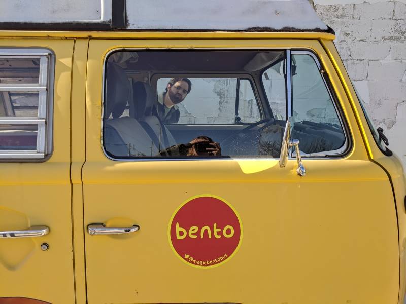 Image: The writer is looking through the driver's side of a yellow Volkswagon bus. The passenger door has a red circle with the word 