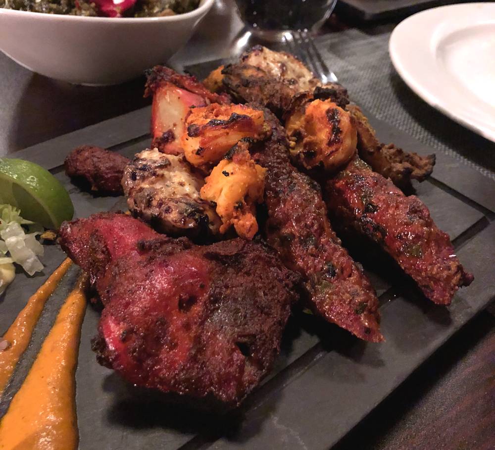 Tandoori Quadruple Play at Himalayan Chimney features griled chicken, shrimp, and kebabs. The meat is marinated in something red, leaving a dark red, grill-charred flesh. It is served on a black slate platter. Photo by Jessica Hammie. 