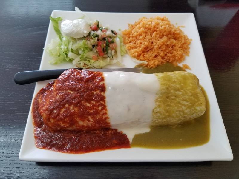 Viva Mexico burrito at La Mixteca. It's served on a square white plate with a steak knife, small salad consisting of shreded lettuce, pico de gallo, and sour cream, and a side of rice. The burrito is enrobed in three sauces: on the left a red sauce, in the middle a white cheese sauce, and on the right a green sauce. Photo by Matthew Macomber. 
