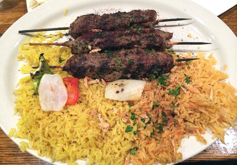 Kufta platter at Layalina restaurant in 2014. On an oval white plate is yellow rice, reddish rice, and three kufta skewers. There are also some grilled peppers and onions. Photo by Jessica Hammie. 