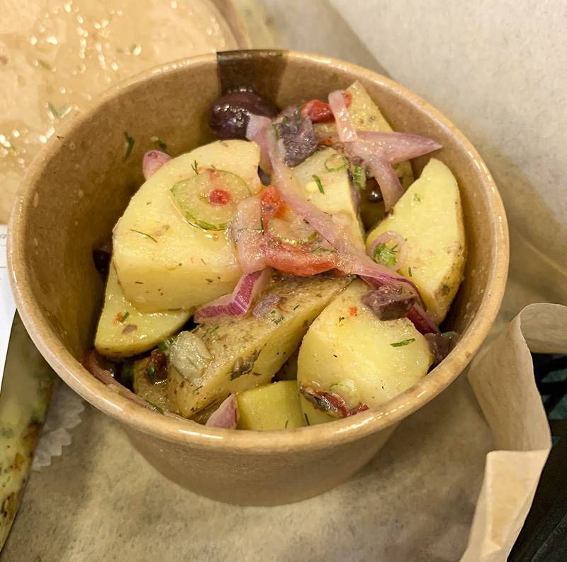 Image: Medterranean potato salad at Baldarotta's served in a brown paper cup. Inside are large pieces of potatoes, sliced red onion, kalamata olives, and chopped roasted red peppers. Photo by Zoe Valentine. 