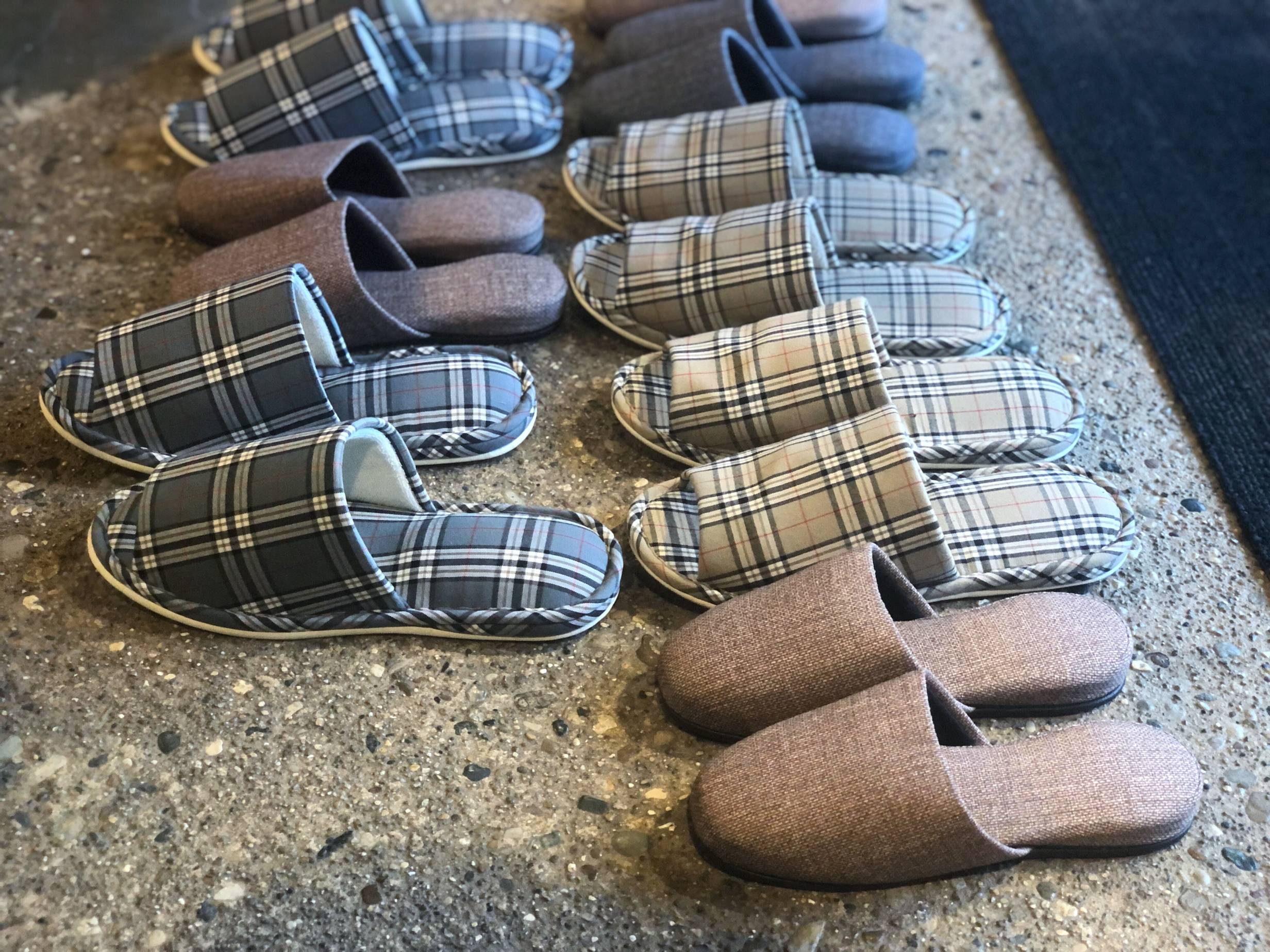 Pairs of slippers, plaid and plain, lined up on spotty floor. Photo by Alyssa Buckley.