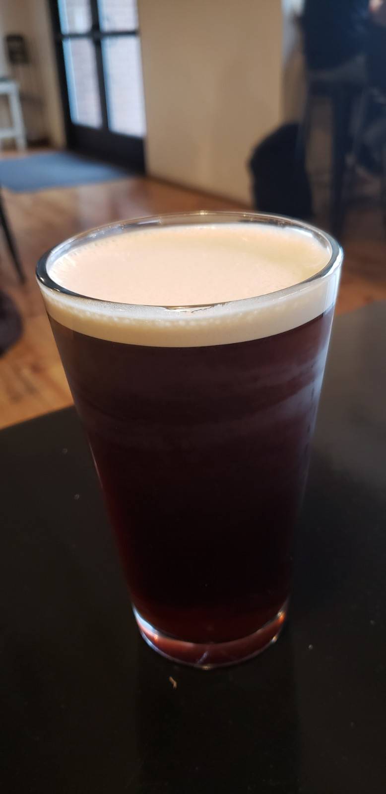 Nitro coffee from Cafeteria & Company. A cold coffee is served in a pint glass. It is a reddish brown color with a cream-colored foam on top. Photo by Elaine Sine. 