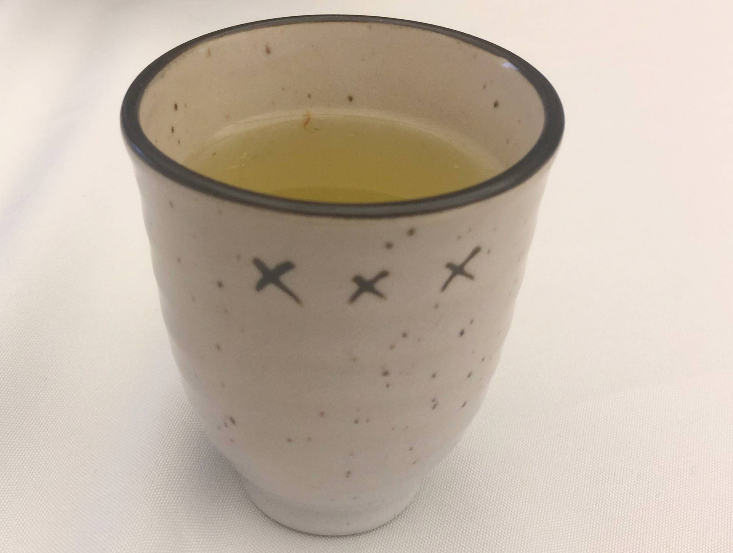 A white ceramic cup with a brown lip is mostly full of a lemonade drink.