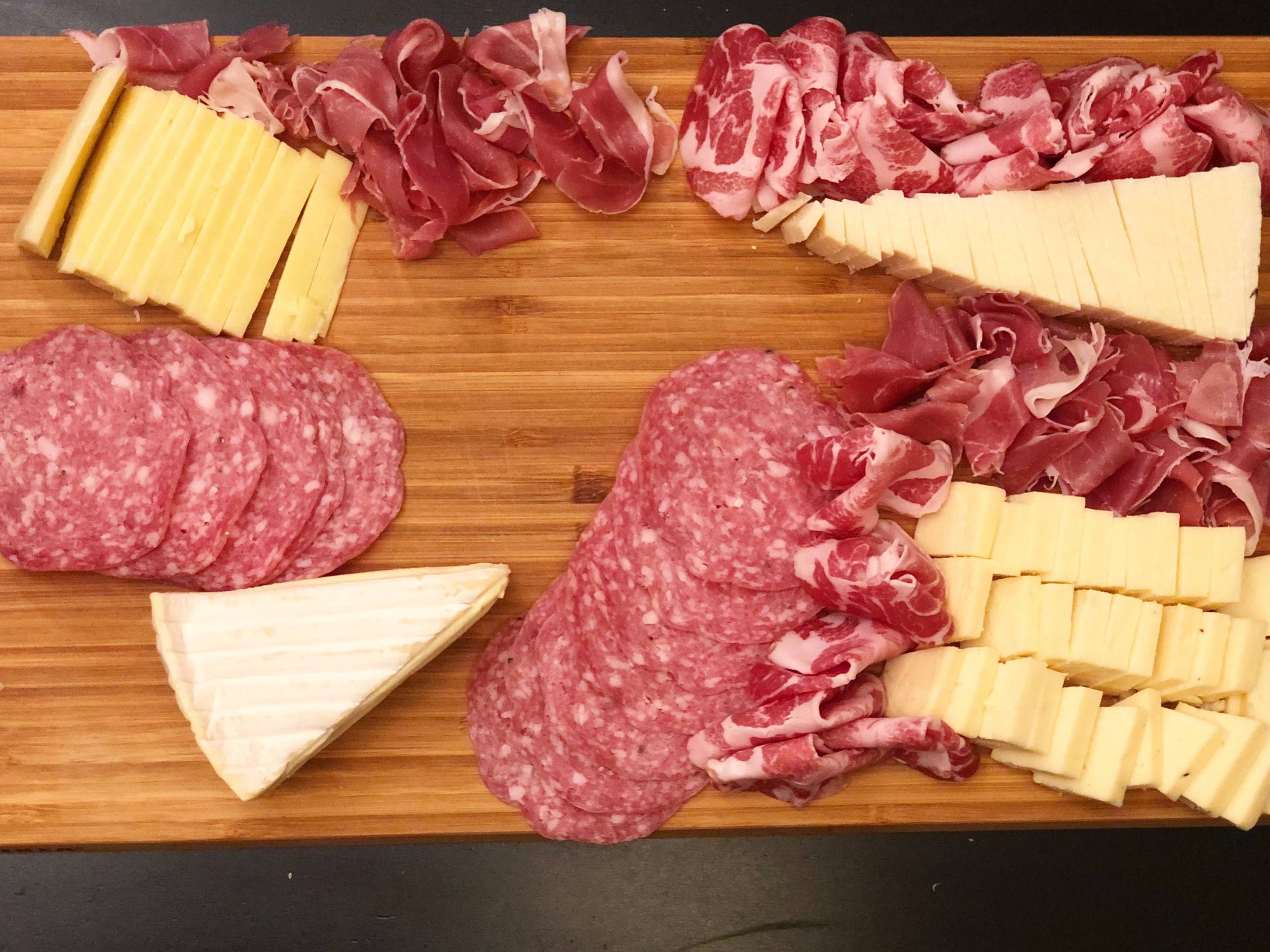 A wooden cutting board with sliced cheese and red meats spread across the board with space left open. Photo by Alyssa Buckley.