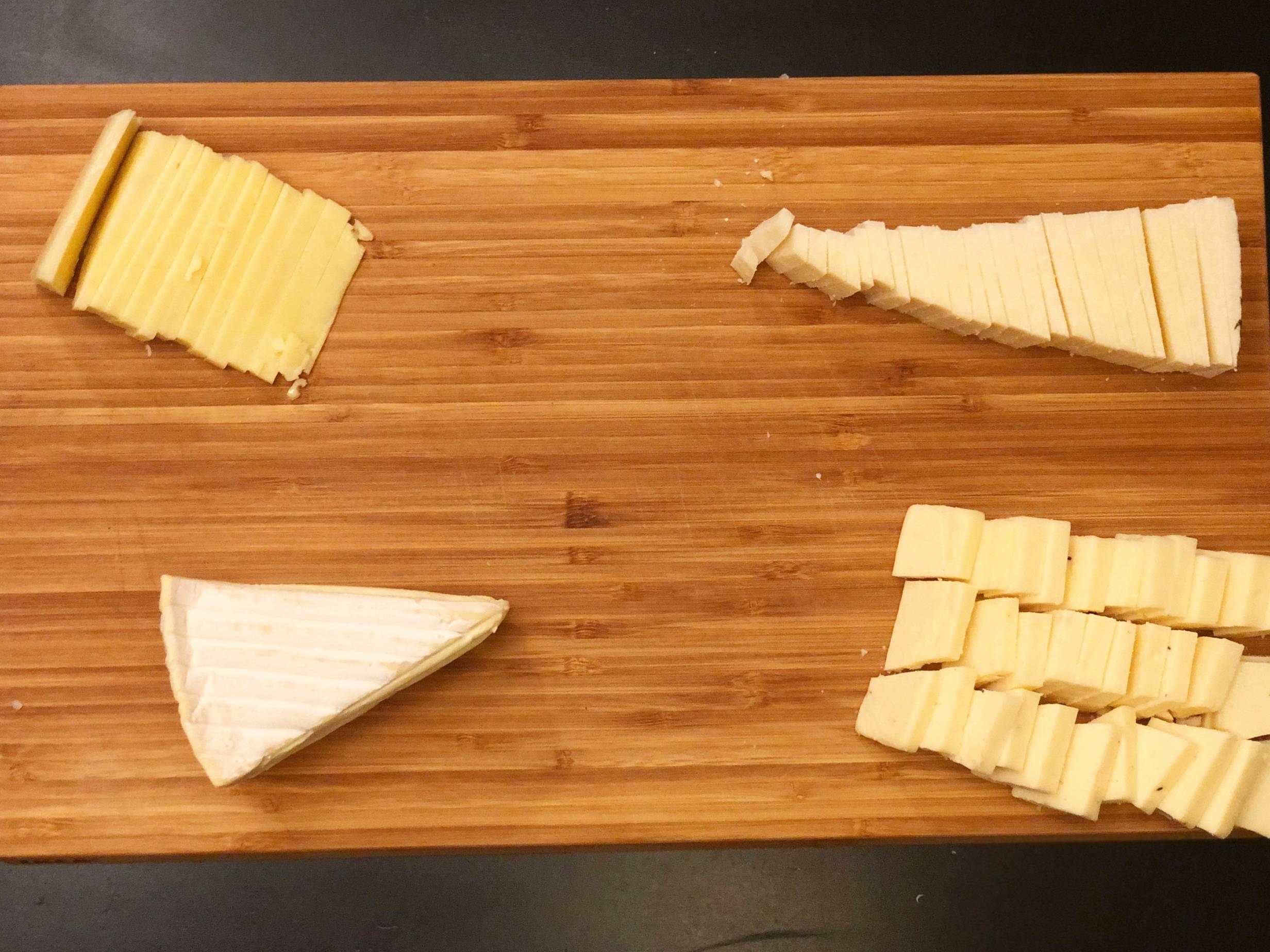 A wooden cutting board with four cheeses. They are all cut into bite sized slices except the Fromager dâ€™Affinois on the bottom left, left in a wedge. Photo by Alyssa Buckley.