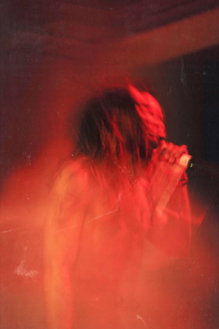 A blurry, red tinted photo that shows a distorted image of a shirtless man rapping on stage.