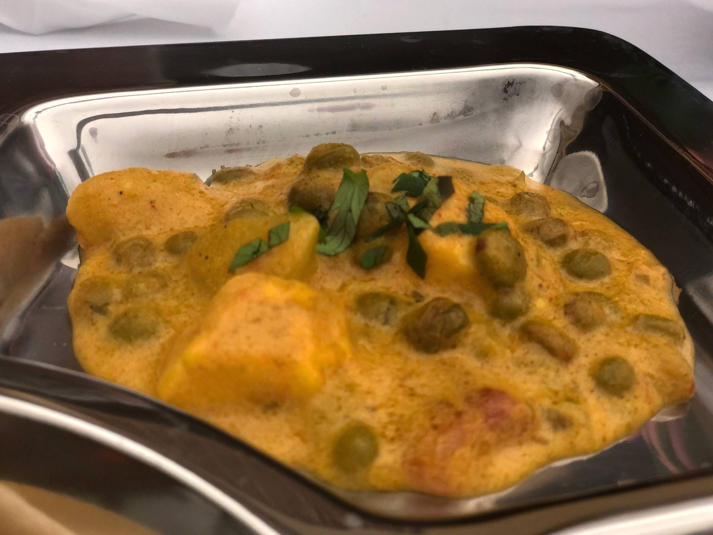 Pigeon peas, potato, and paneer in a yellow thick sauce in a divider of a metal tray. Photo by Alyssa Buckley.
