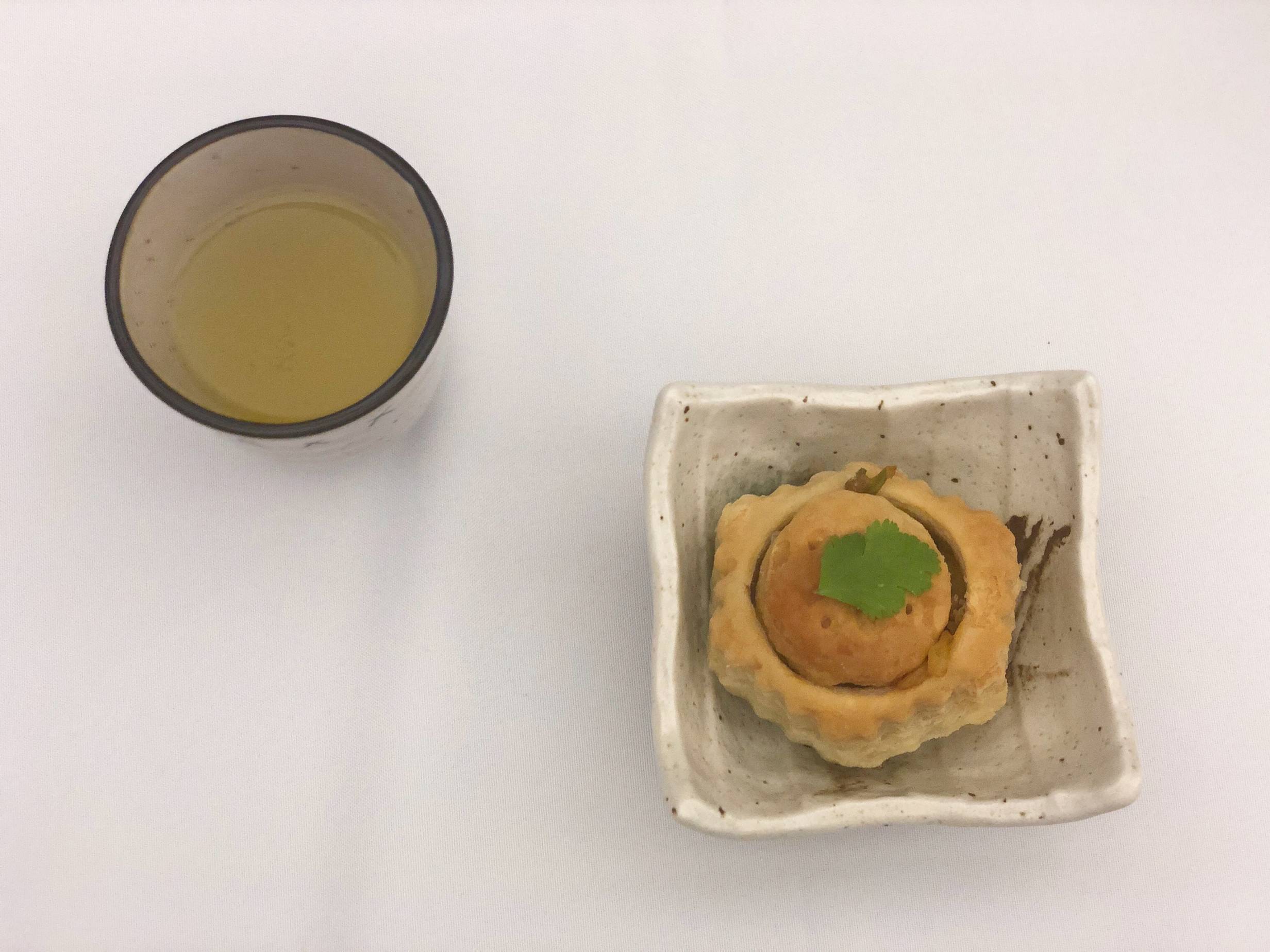 An overhead shot of a ceramic cup with lemonade and a square plate with a vegetable puff. Both are on a table with a white tablecloth. Photo by Alyssa Buckley.