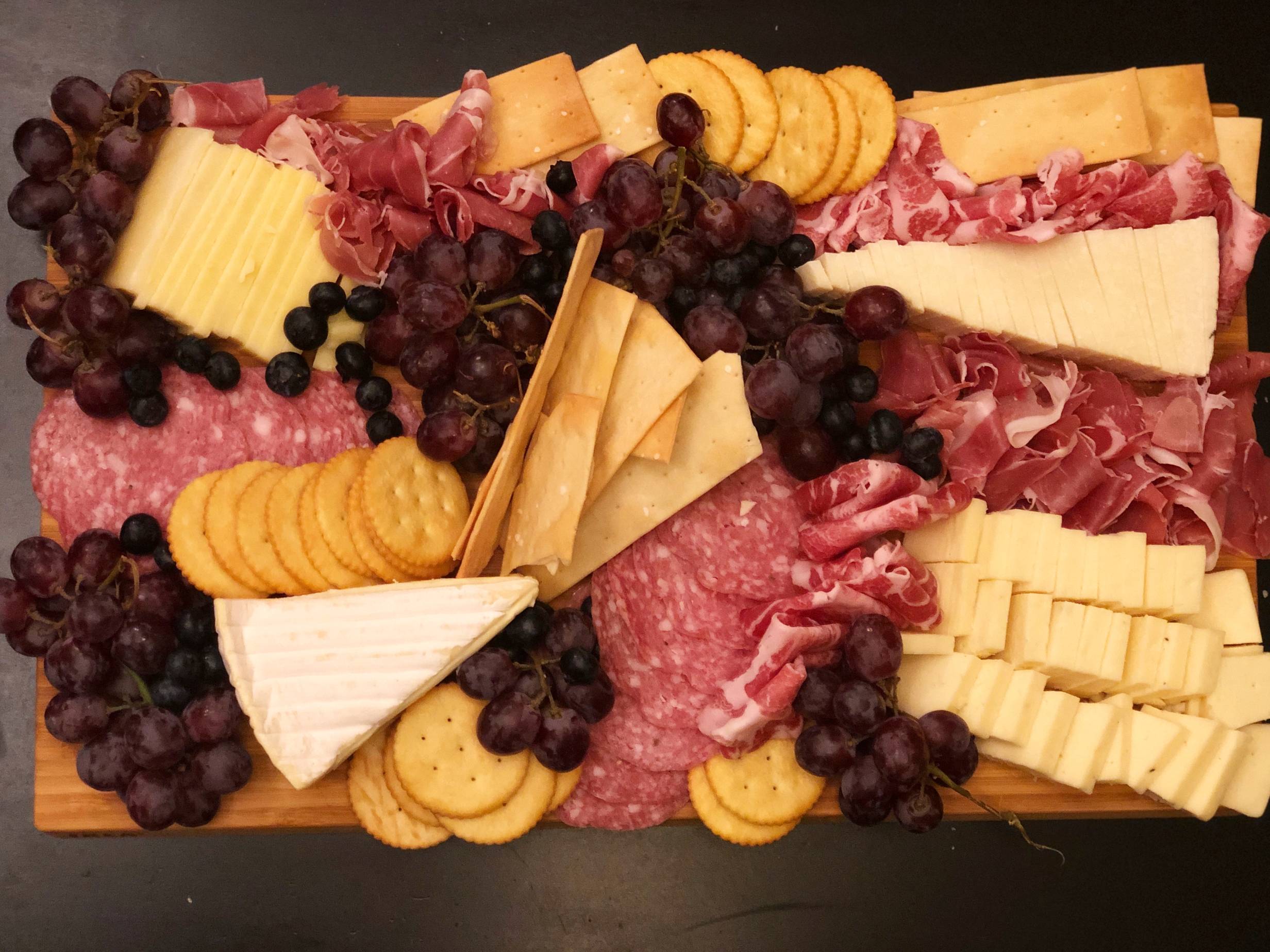 Salami, dry coppa, proscuitto, four kinds of cheese, grape clusters, and blueberries on a wooden cutting board. Photo by Alyssa Buckley.