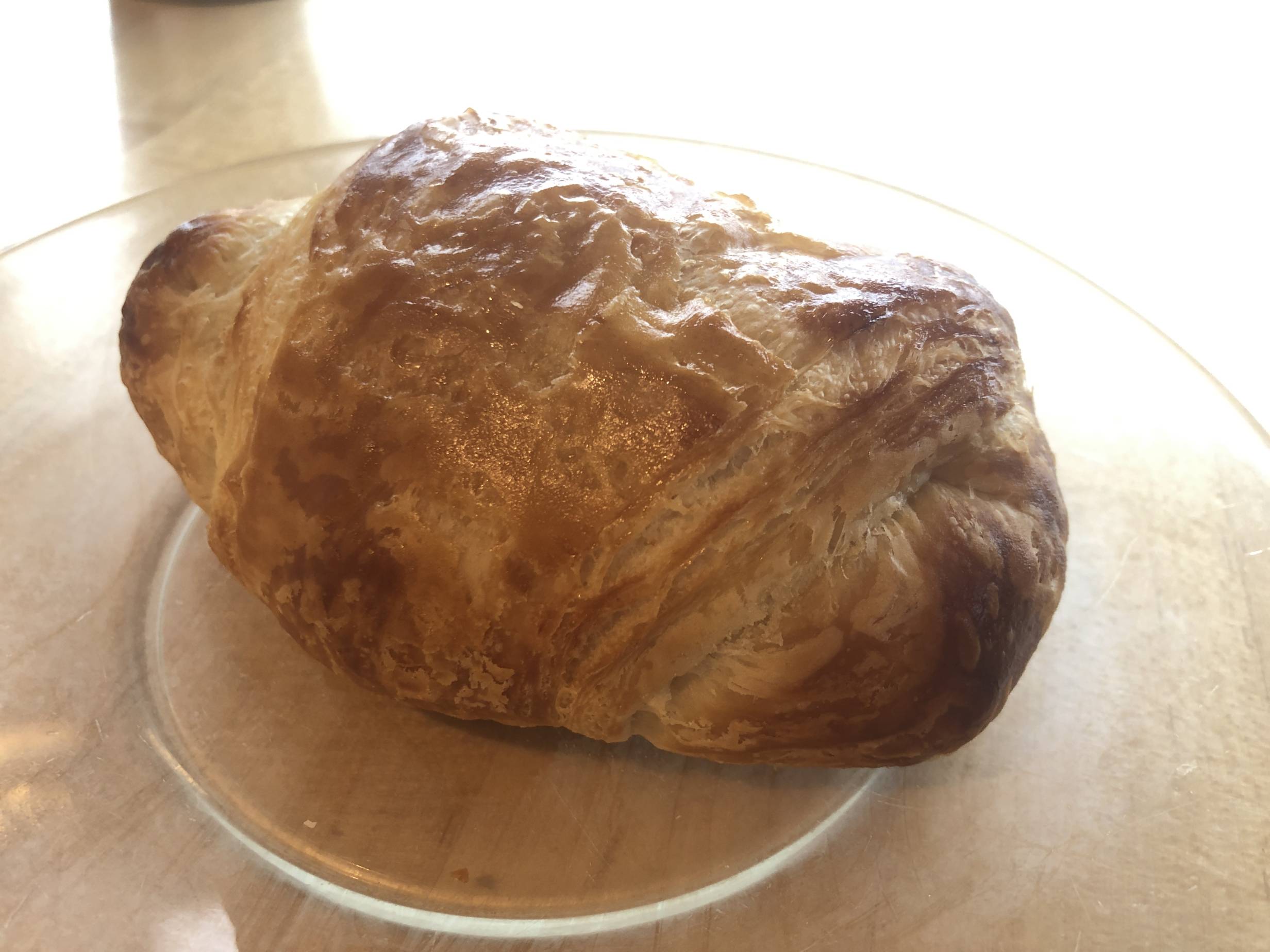 A lightly toasted croissant sits on a small glass plate on a wooden table at Art Mart. Photo by Alyssa Buckley.