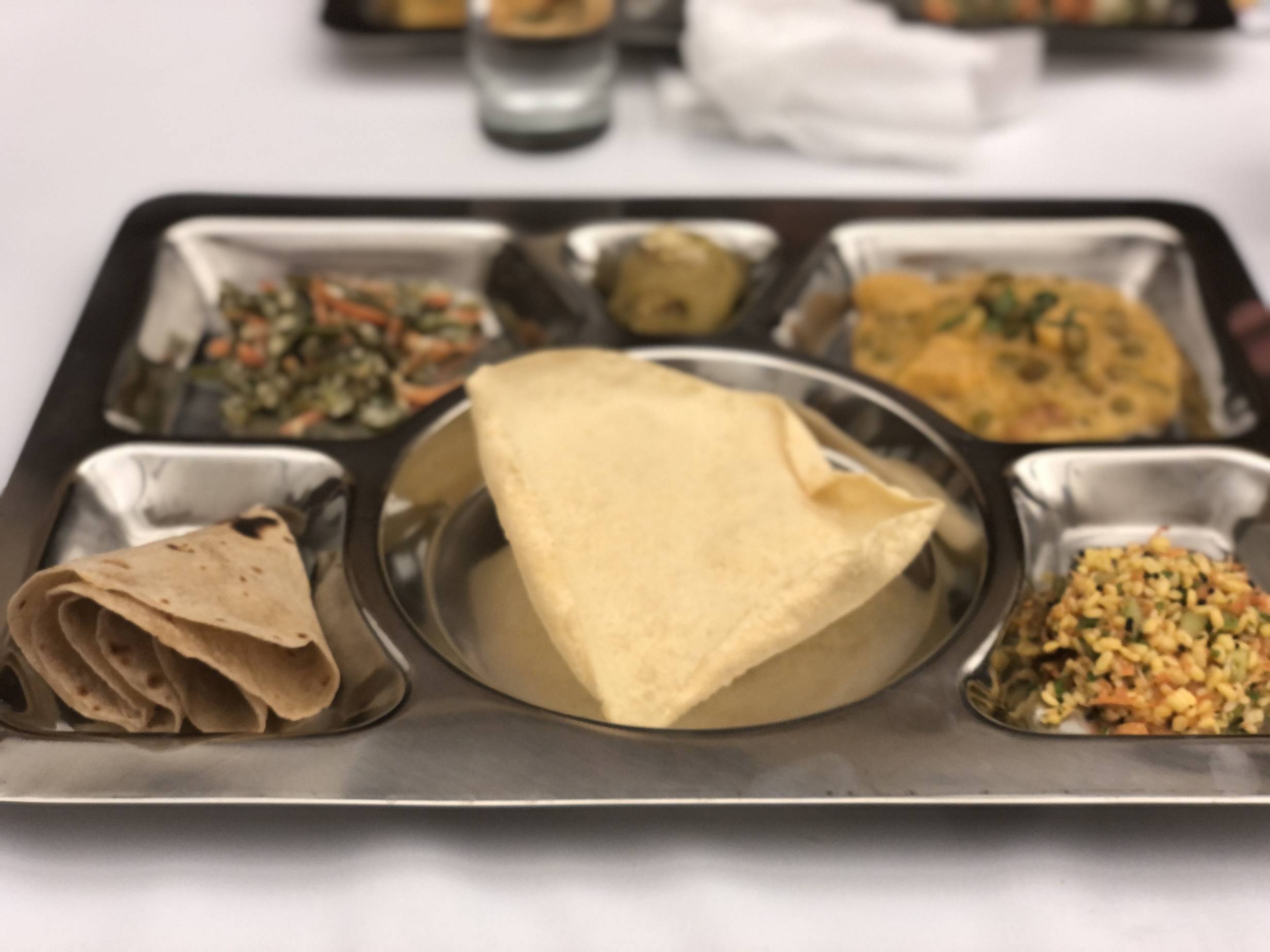 A metal tray with palya, korma, kesari bath, kosambri, papad, and chapatti. Photo by Alyssa Buckley.