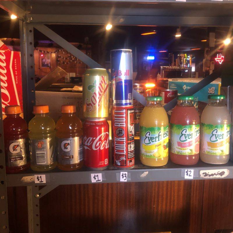 A metal shelf with individual bottles of Gatorade, cans of soda and Red Bull, and bottles of Everfresh juice.