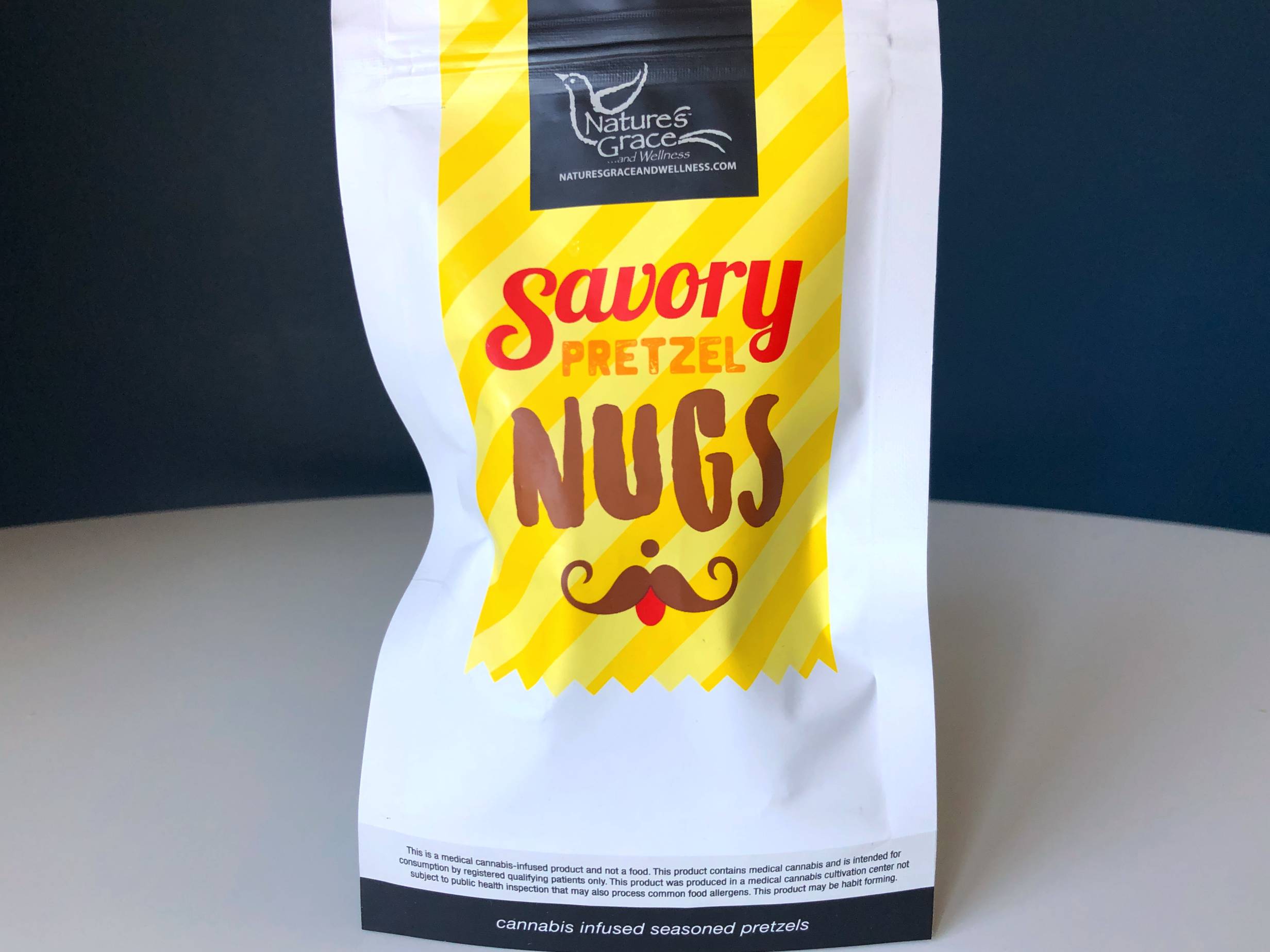 A top-zip bag of Nature's Grace Savory Pretzel Nugs sits on a white table with a blue background. Photo by Alyssa Buckley.