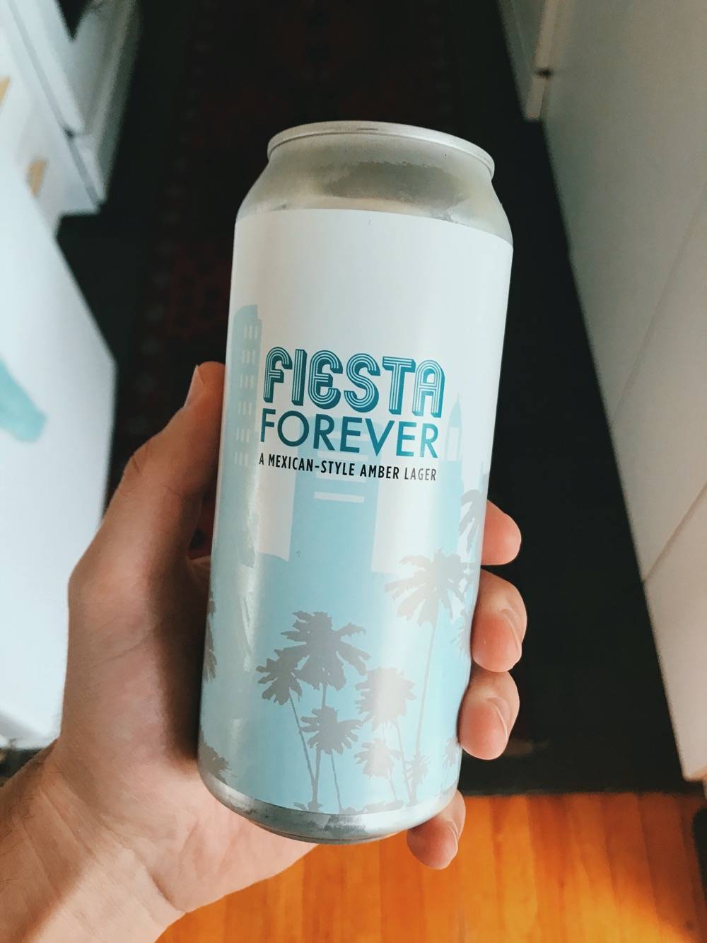 IMAGE: A can of beer being held in a hand. Label says FIESTA FOREVER: A Mexican Style Amber Lager. Photo by Patrick Singer.