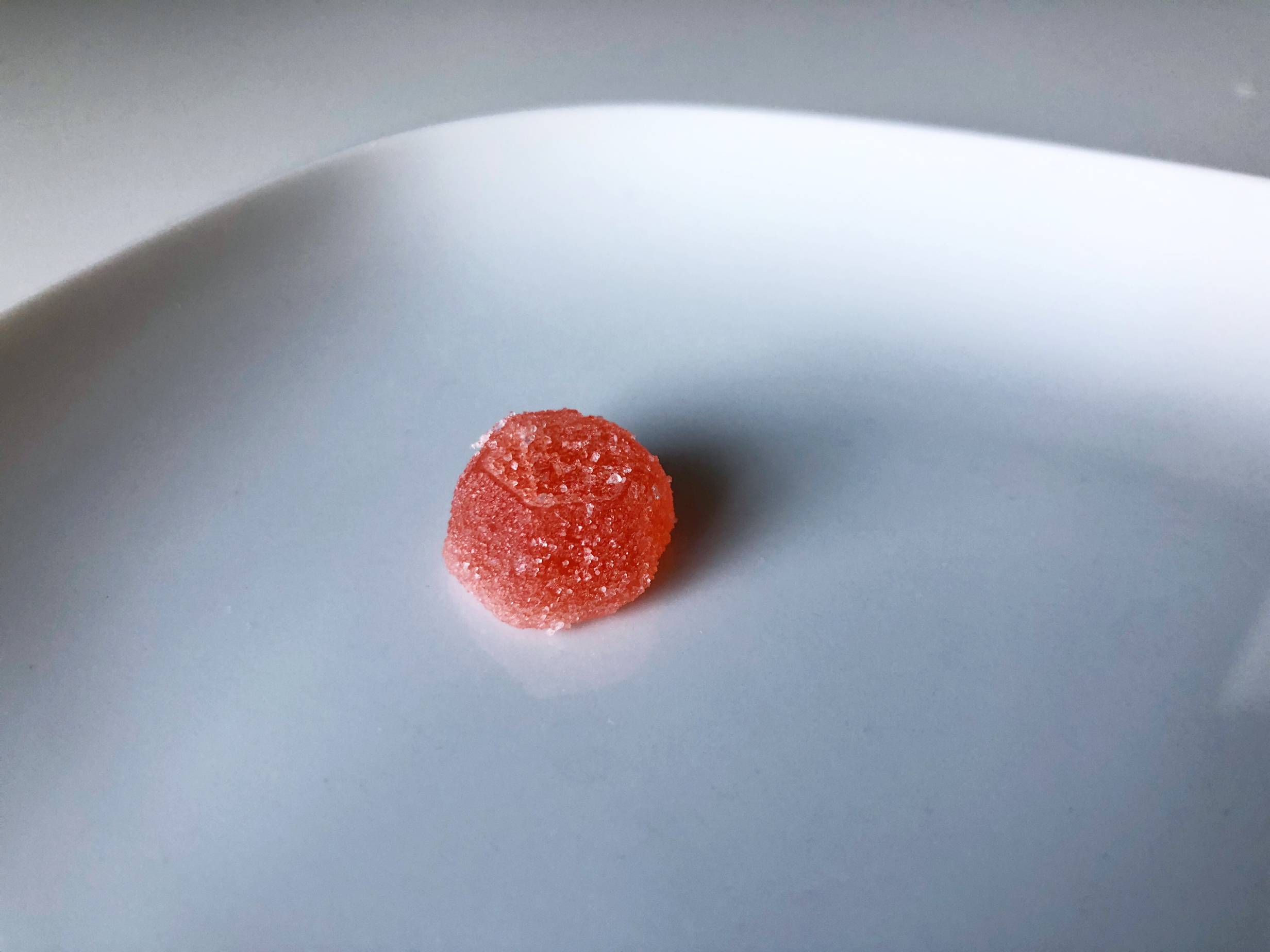 A round, spherical orange gummy covered in sugar sits on a white plate. Photo by Alyssa Buckley.