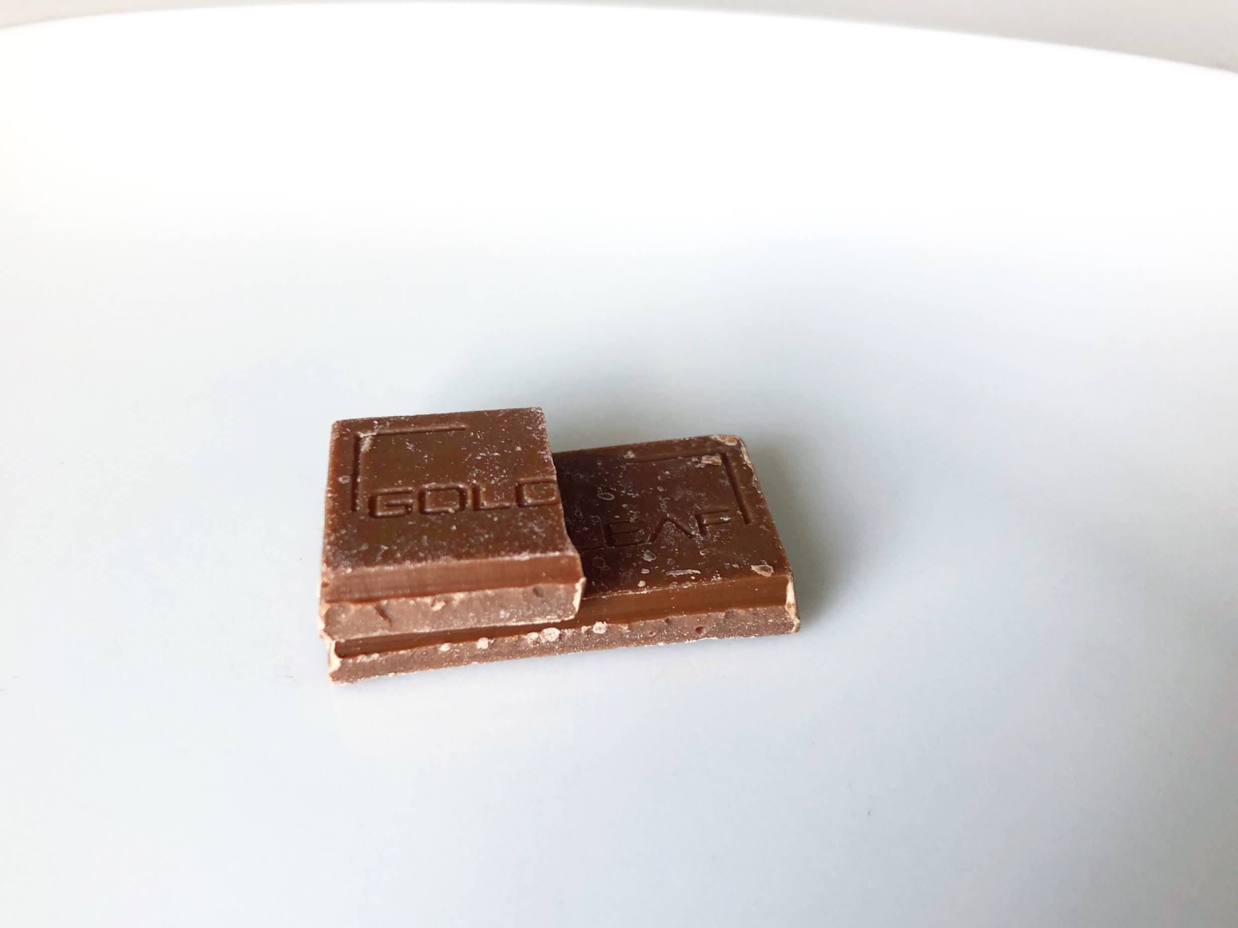 Two small cannabis-infused chocolate rectangles sit on a plate. The top one is cut in half, and missing half. The bottom is a full rectangle bar of chocolate. Photo by Alyssa Buckley. 