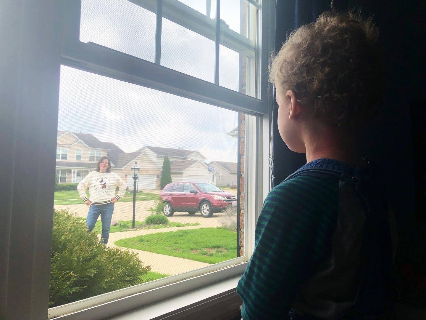 A child looks out the window to see a teacher in a Mickey sweatshirt on the front walk near the grass. Photo by Alyssa Buckley.