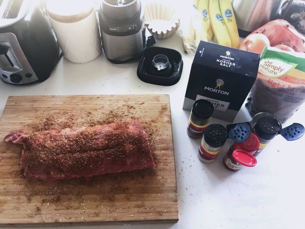 IMAGE: A countertop with a slab of ribs on the left, and seasonings and salts on the right. A bunch of bananas sit in the background. Photo by Patrick Singer.