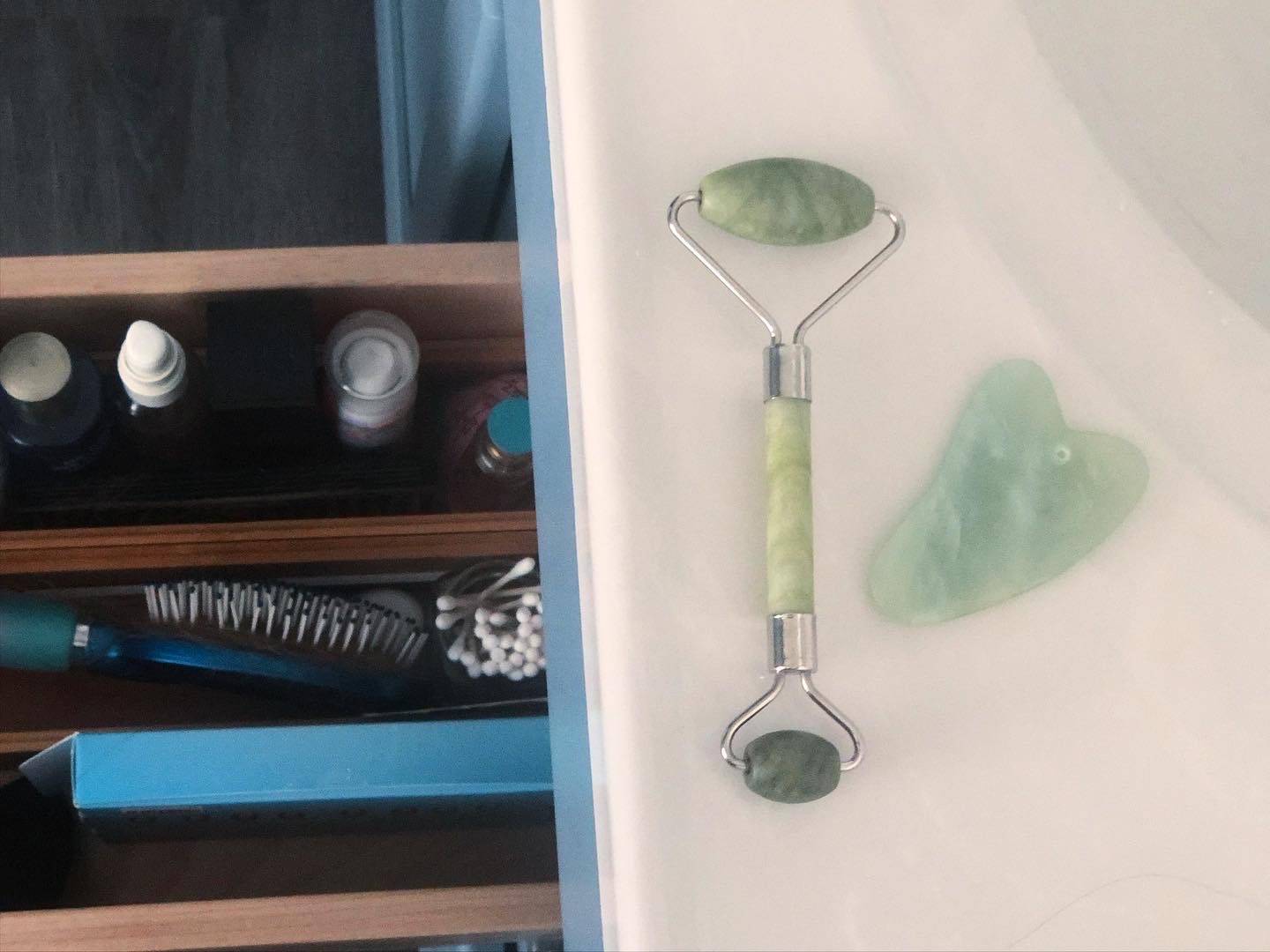 A jade rollers sits on a white bathroom counter. A drawer is open revealing a variety of personal hygiene items. Photo by Alyssa Buckley.