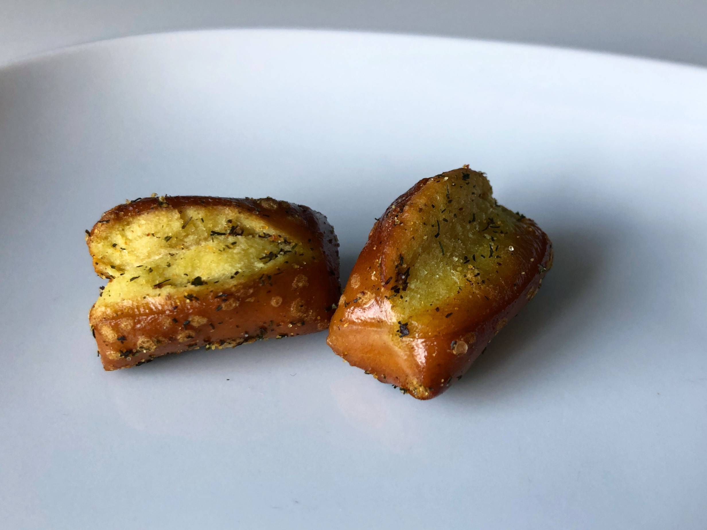 Two small cannabis-infused pretzel bites with bits of herbs and salt sit on a white plate. Photo by Alyssa Buckley.