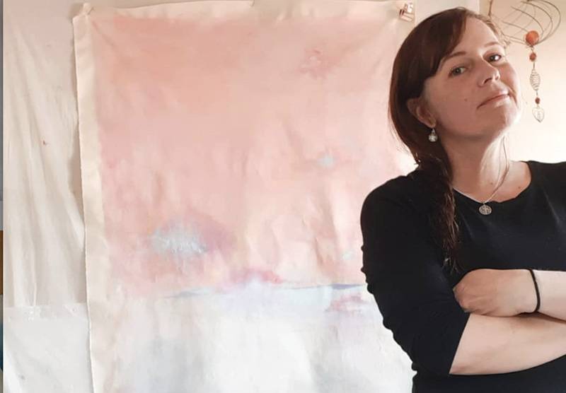 Image: Photo of artist Carol Farnum standing in front of canvas with pale pink paint. Photo from Instagram