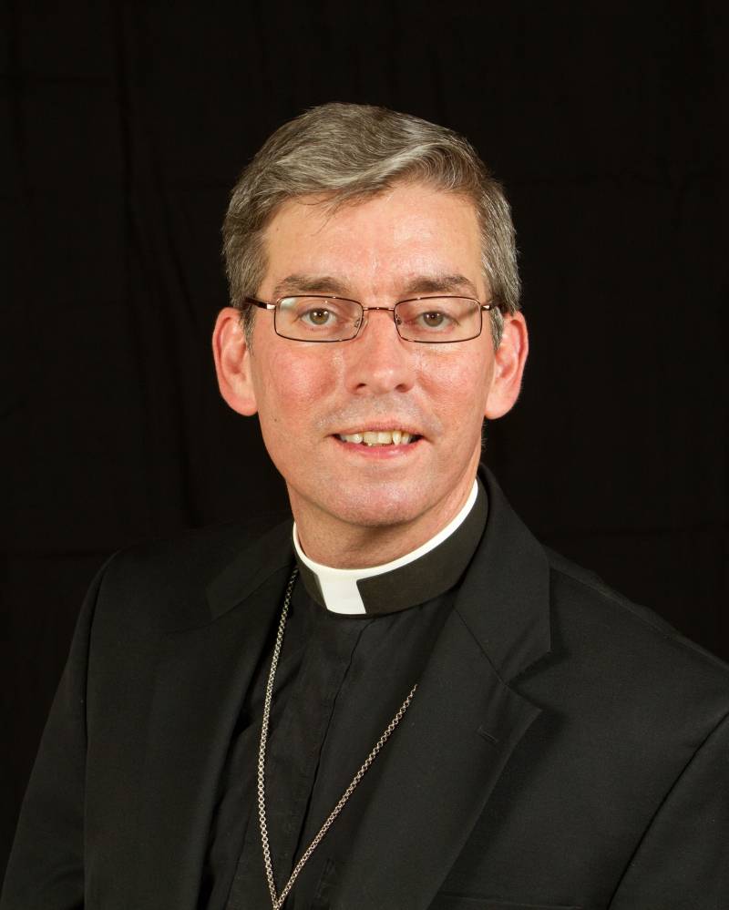 A headshot of a man with gray hair and glasses. He is wearing a black shirt and jacket and a white clerical collar. Photo provided by Pastor Chris Repp.