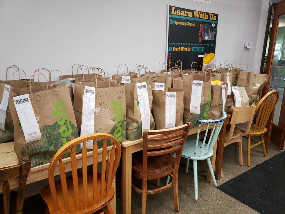 Several paper bags with receipts attached are lined up along a wooden table with chairs pushed in. Photo by Common Ground Food Co-op Facebook page.