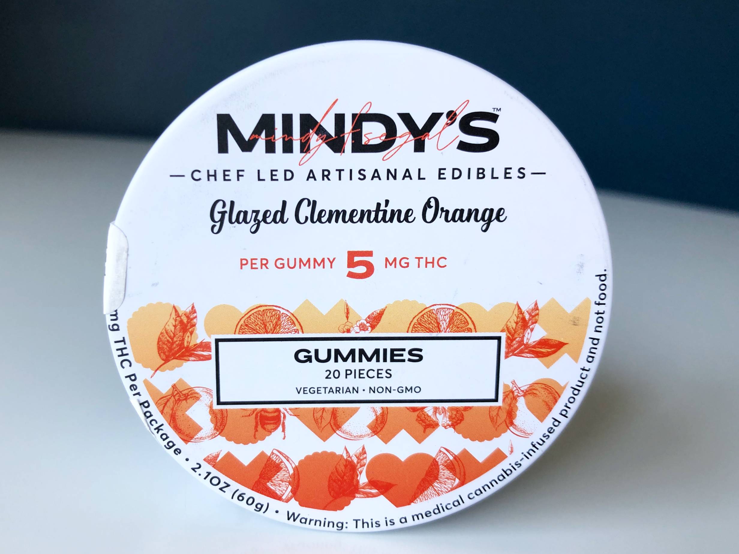 A round, metal tin is balanced on its side to show the top of the tin with all the brand and gummy information for Mindy's Glazed Clementine Orange gummies. Photo by Alyssa Buckley.