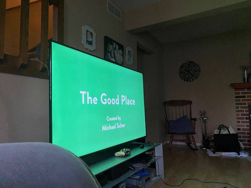 A Tl.V. screen with a green background. It says The Good Place in white text. In the background is a rocking chair and fireplace utensils. Photo by Julie McClure. 