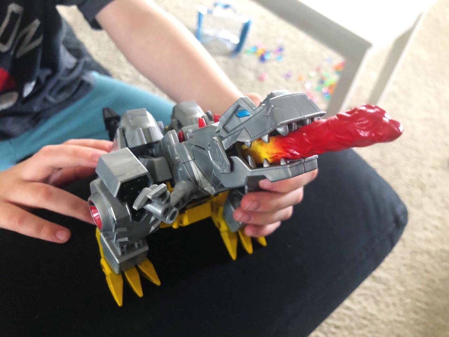 A gray, plastic dragon transformer toy is being played with by a child on a black couch. Only the child's hands are visible. Photo by Alyssa Buckley.