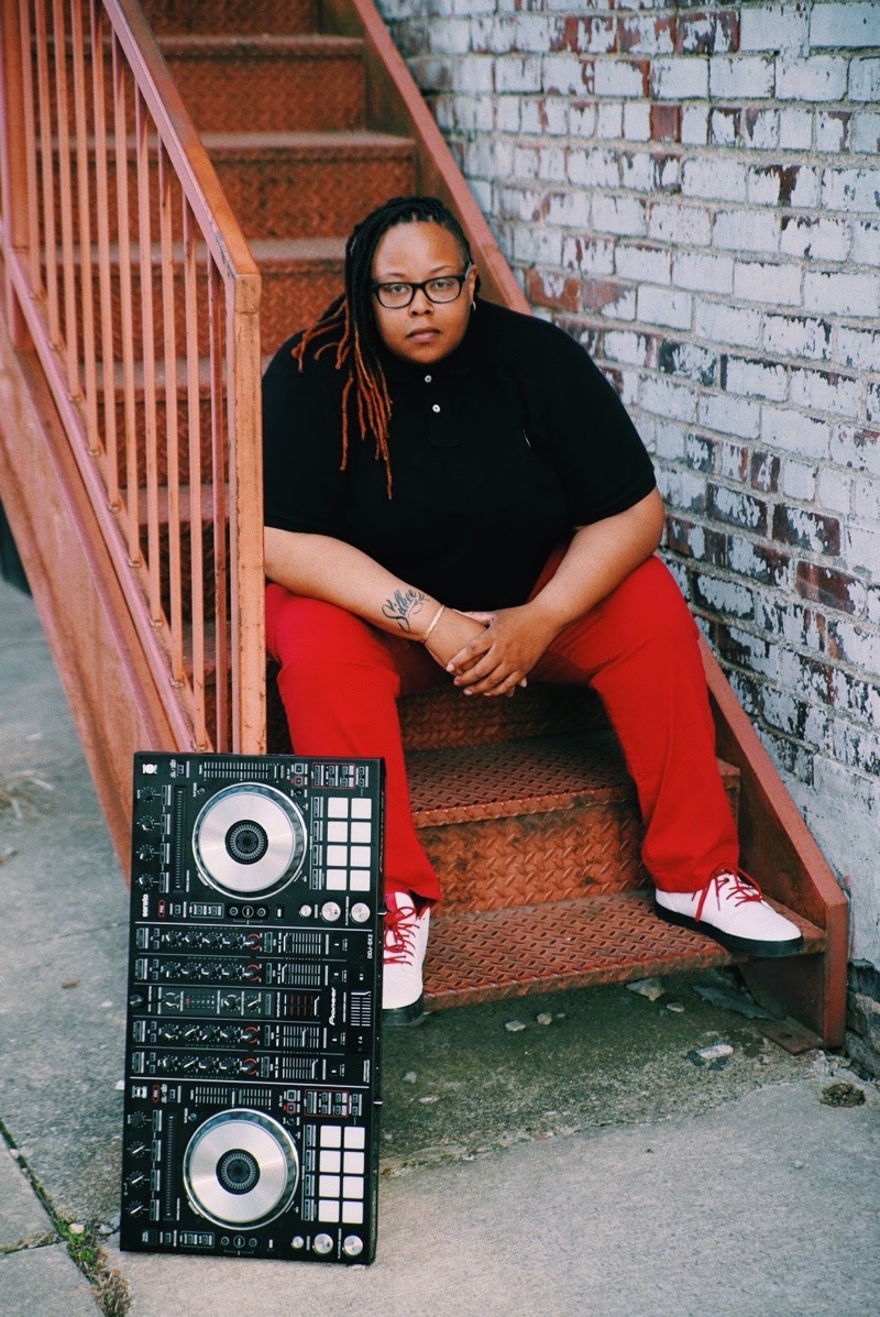 IMAGE: Woman sits on red staircase, wearing a black shirt and red pants. There's a turntable sitting in front of her. Photo by Chad 