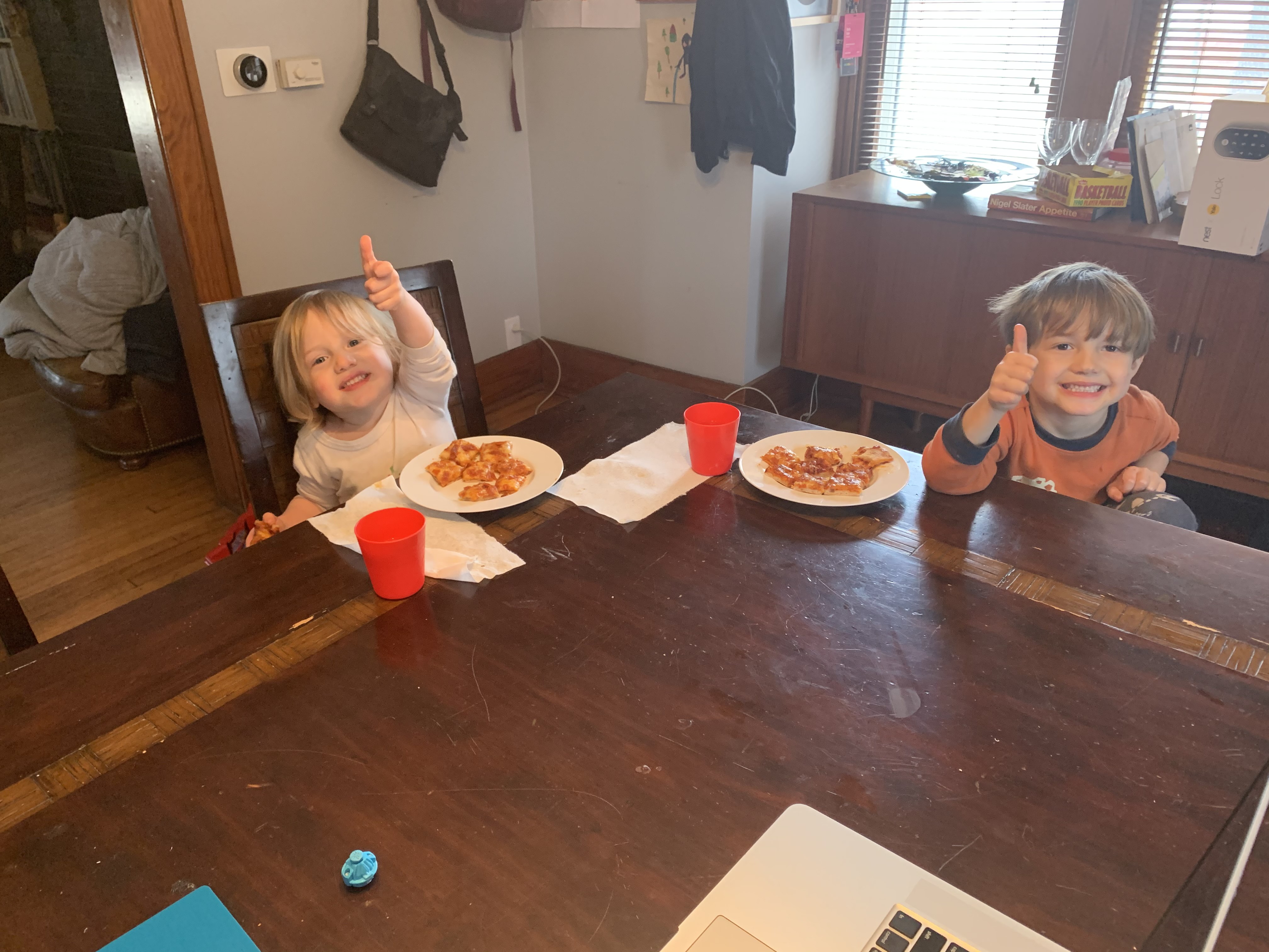 Two young children give a thumbs up as they eat the pizza they helped to make. Photo by Seth Fein 