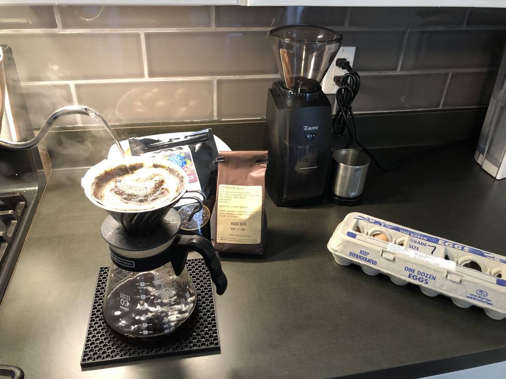 A kitchen counter. A pour-over coffee apparatus is set up, with someone off camera pouring hot water. Behind the coffee pot is a bag of coffee. To the right is a carton of eggs. Photo by Carly McCrory-McKay. 