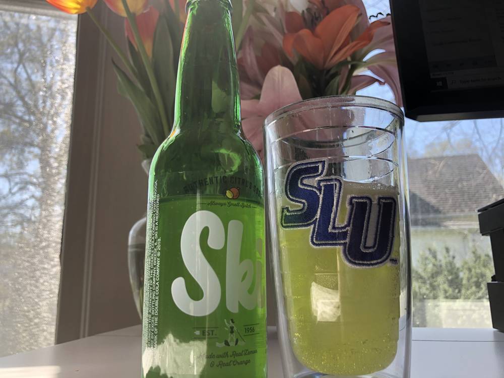A green bottle of Ski soda sits on a desk. To the right, a large tumbler cup with 